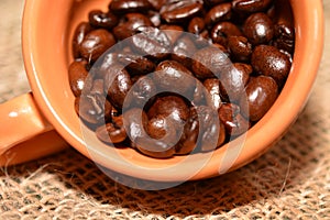 Coffee cup with burlap sack of roasted beans on rustic table