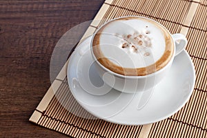 Coffee cup of cappuccino on bamboo mat, on wooden background wit