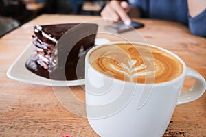 Coffee cup and chocolate cake on wood table background woman use mobile phone in coffee shop.