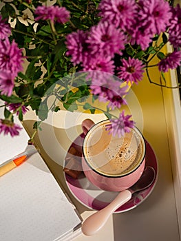 Coffee cup chocolate notebook beautiful pink autumn Chrysanthemum flowers in yellow pot on window. Cozy home