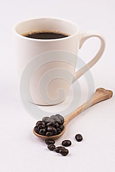 Coffee cup and coffee beans on wooden spoon on white