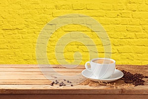 Coffee cup with coffee beans on wooden table over yellow brick stone wall background
