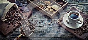 Coffee cup with coffee, coffee beans, cane sugar, muscovado sugar on an old wood desk in a coffee shop. Wide image in retro style