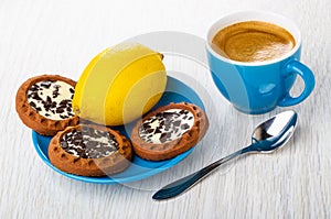 Coffee in cup, cookies with cream, chocolate, lemon on saucer, spoon on table