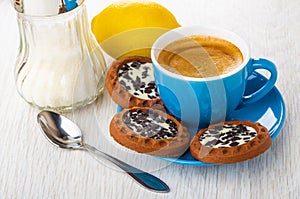 Coffee in cup, cookies with cream, chocolate on saucer, spoon, sugar bowl, lemon on table