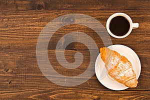 Coffee cup with croissant for breakfast on a dark wooden table, top view