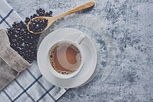 Coffee cup with Dark Roasted coffee beans in bag and wooden spoon on old kitchen table cement top