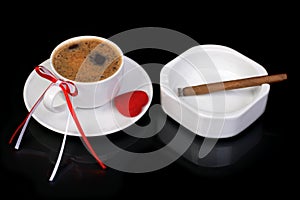 Coffee cup decorated with a bow and heart. Cigar and ashtray on a black background