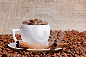 Coffee cup demitasse full of coffee beans and cinnamon sticks in the heap coffee beans photo