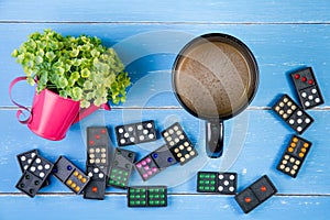 Coffee cup, Domino and plastic flowers on the blue wooden background.