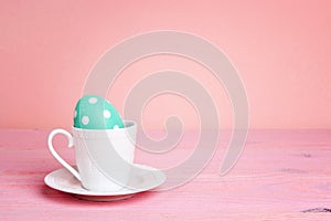 Coffee cup with Easter egg on a pink table.