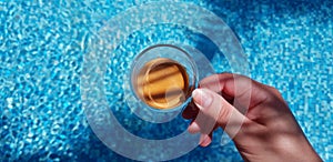 Coffee cup in female hand over blue waters in the pool