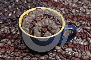 A coffee cup filled to the brim with roasted coffee beans sits in the middle of scattered coffee beans with the texture of an Amer