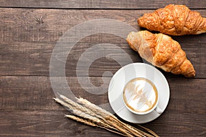 Coffee cup and fresh baked croissants on wooden background. Top