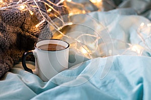 Coffee cup and garland on a bed. Atmospheric hygge style. Cozy winter or autumn concept