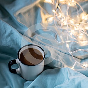 Coffee cup and garland on a bed. Atmospheric hygge style. Cozy winter or autumn concept