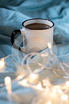 Coffee cup and garland on a bed. Atmospheric hygge style. Cozy winter or autumn concept