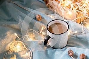 Coffee cup and garland on a bed. Atmospheric hygge style. Cozy winter or autumn concept