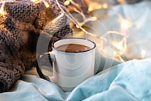 Coffee cup and garland on a bed. Atmospheric swedish hygge style. Cozy winter or autumn morning