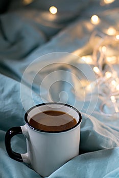 Coffee cup and garland on a bed. Atmospheric swedish hygge style. Cozy winter or autumn morning