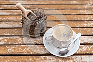 Coffee cup with glass jar filled with coffee beans on a wooden garden table.