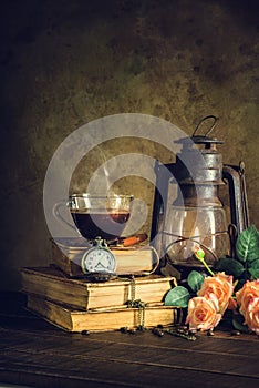 Coffee in cup glass on old books and clock vintage with kerosene lamp oil lantern burning with glow soft light on aged wood floor