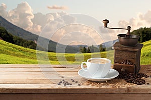 Coffee cup with grinder mill on wooden table over beautiful land