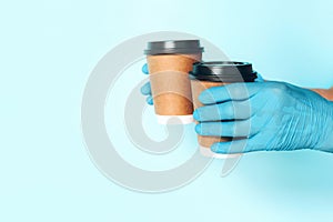 Coffee cup in hand with medical glove on blue background. Banner with copy space. Contactless delivery service during quarantine