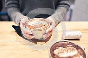 Coffee cup between hands in cafe in winter. Cappuccino, macchiato, latte or hot chocolate cocoa. Two persons having a warm meeting photo