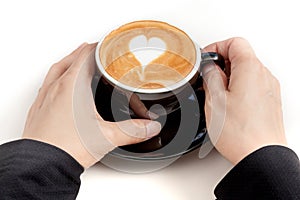 Coffee cup with heart shape latte art on top, hand holding the c