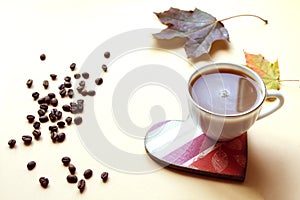 Coffee Cup on a heart - shaped stand with scattered coffee beans and maple leaves,close-up, side view-coffee Day celebration