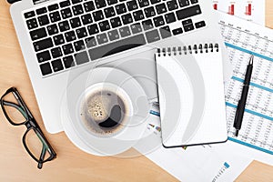 Coffee cup, laptop and notepad over papers with numbers and char