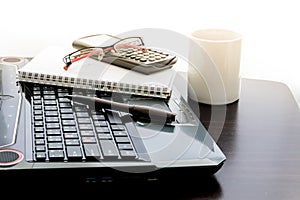 Coffee cup, laptop, pen , Calculator , notepad and glasses on wooden table