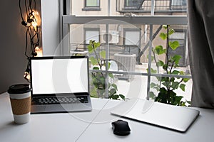 Coffee cup and laptop on the table with window background.
