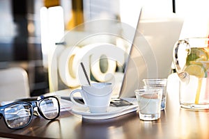 Coffee cup, lemonade, eyeglasses and laptop laid on table.