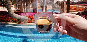 Coffee cup made from transparent glass in female hand against blue outdoor pool