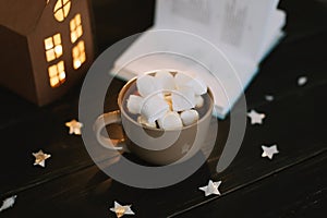 Coffee cup with marshmallows and a book on the table. Still life on dark background.