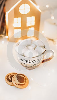 Coffee cup with marshmallows and cookies on bokeh lights background. Christmas and New Year cozy still life lights and decorations