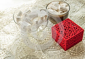 Coffee cup with marshmallows  glass bowl with marshmallows  red ring box on beige lace tablecloth  vintage  romance  surprise
