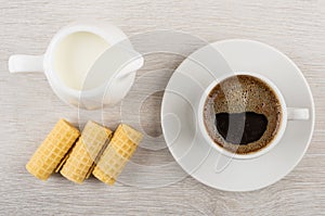 Coffee cup, milk in jug, wafer rolls on wooden table