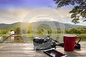 Coffee Cup with mobile phone and camera  on wood table over mountains landscape with sunlight vintage