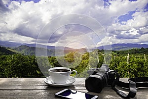 Coffee Cup with mobile phone and camera  on wood table over mountains landscape with sunlight vintage.