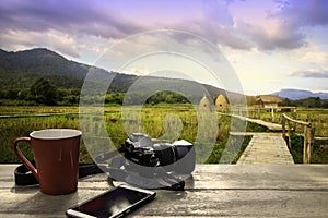 Coffee Cup with mobile phone and camera on wood table over mountains landscape with sunlight vintage