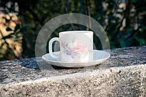 Coffee cup in morning sunlight. Summer fresh cool look. White coffee cup on saucer for hot drink on roof beam of a residential