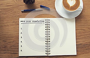 Coffee cup and notebook with new years resolution on rustic desk photo