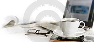 Coffee cup on an office desk with cell phone, laptop, glasses an