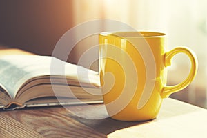 Coffee cup and open book on wooden table, morning sunlight background