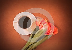 Coffee cup and orange tulip flowers on wooden background.