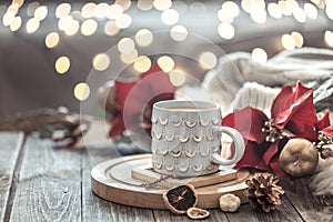 Coffee cup over Christmas lights bokeh in home on wooden table with flowers on a background and decorations. Holiday decoration,