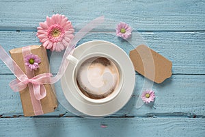 Coffee cup, pink flowers and a gift on pastel blue wood backgrou